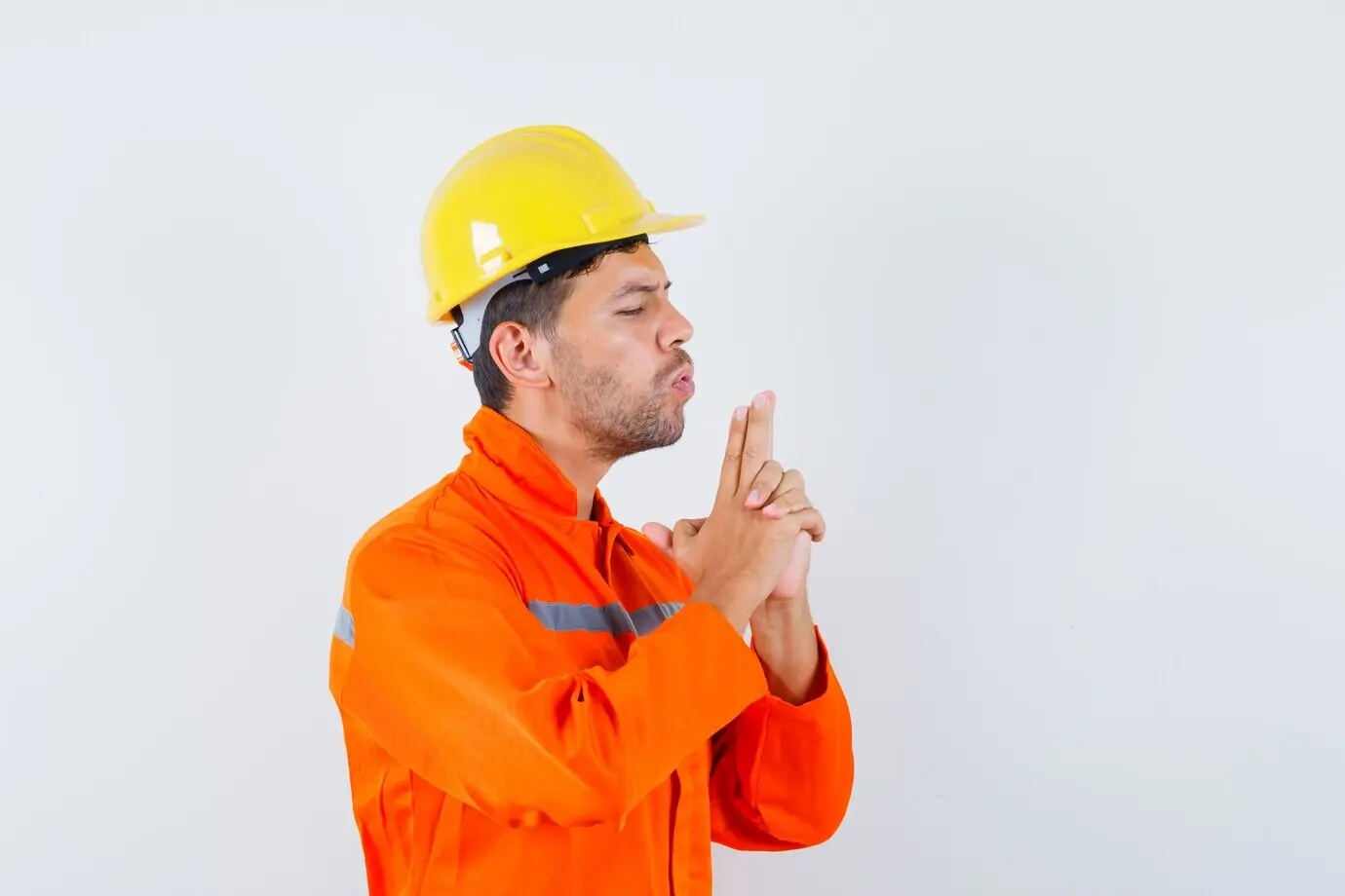 Молодой рабочий, одетый в форму и каску, дует на сложенный из пальцев пистолет и выглядит уверенно.