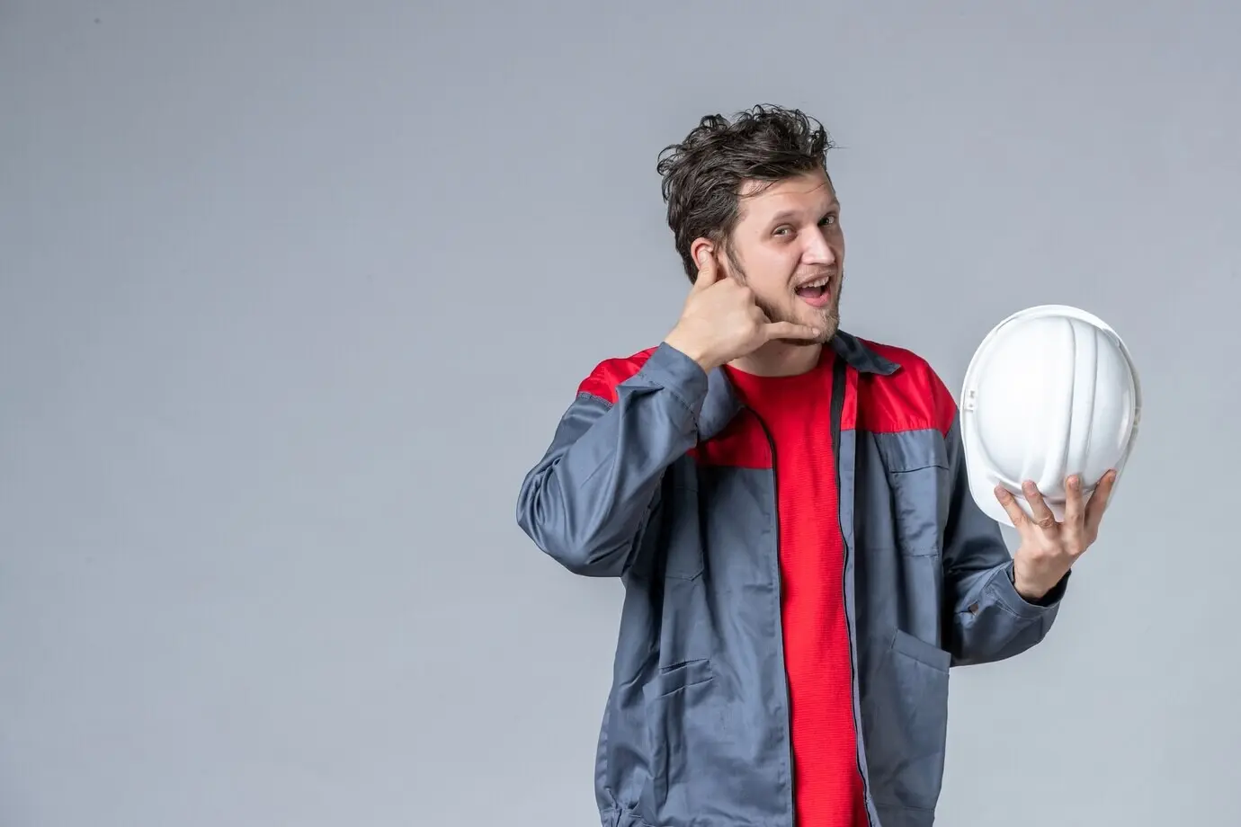 Вид спереди: мужчина-строитель в униформе держит шлем на светлом фоне.